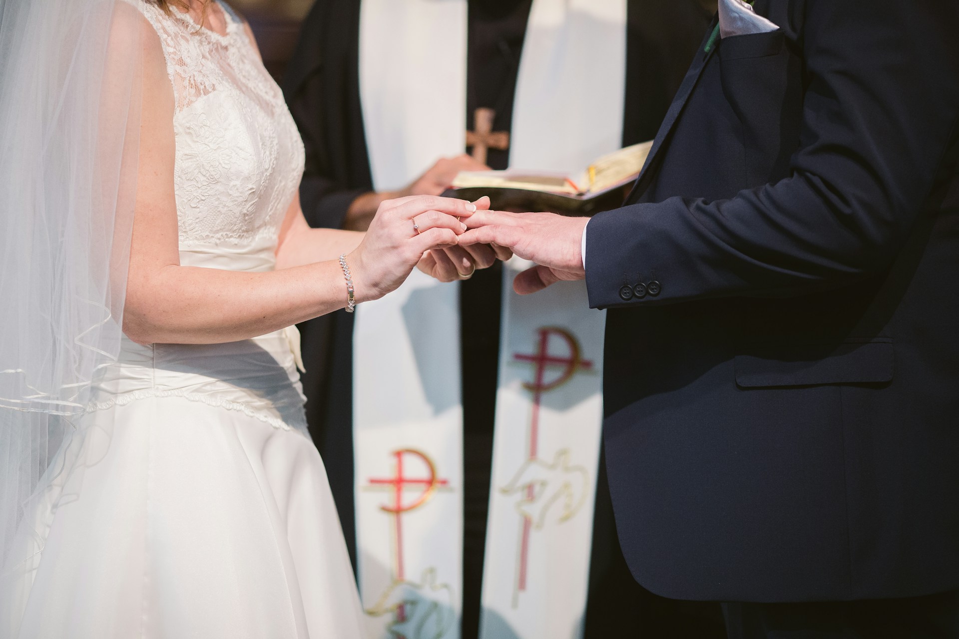 Bride placing a ring on the groom's finger before a priest, during a wedding ceremony.